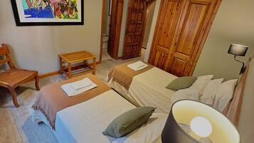 A bedroom with two beds, a wooden chair, a small table, a painting, and a lamp.
