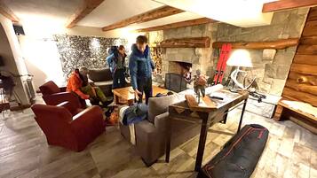 A cozy living room with a stone fireplace, wooden beams, and a ski rack.