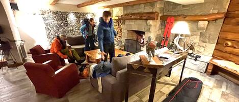 Una sala de estar acogedora con chimenea de piedra, vigas de madera y un soporte para esquíes.