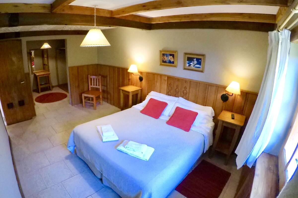 Una habitación con una cama, dos mesitas de noche, una silla, una pequeña mesa y una lámpara.