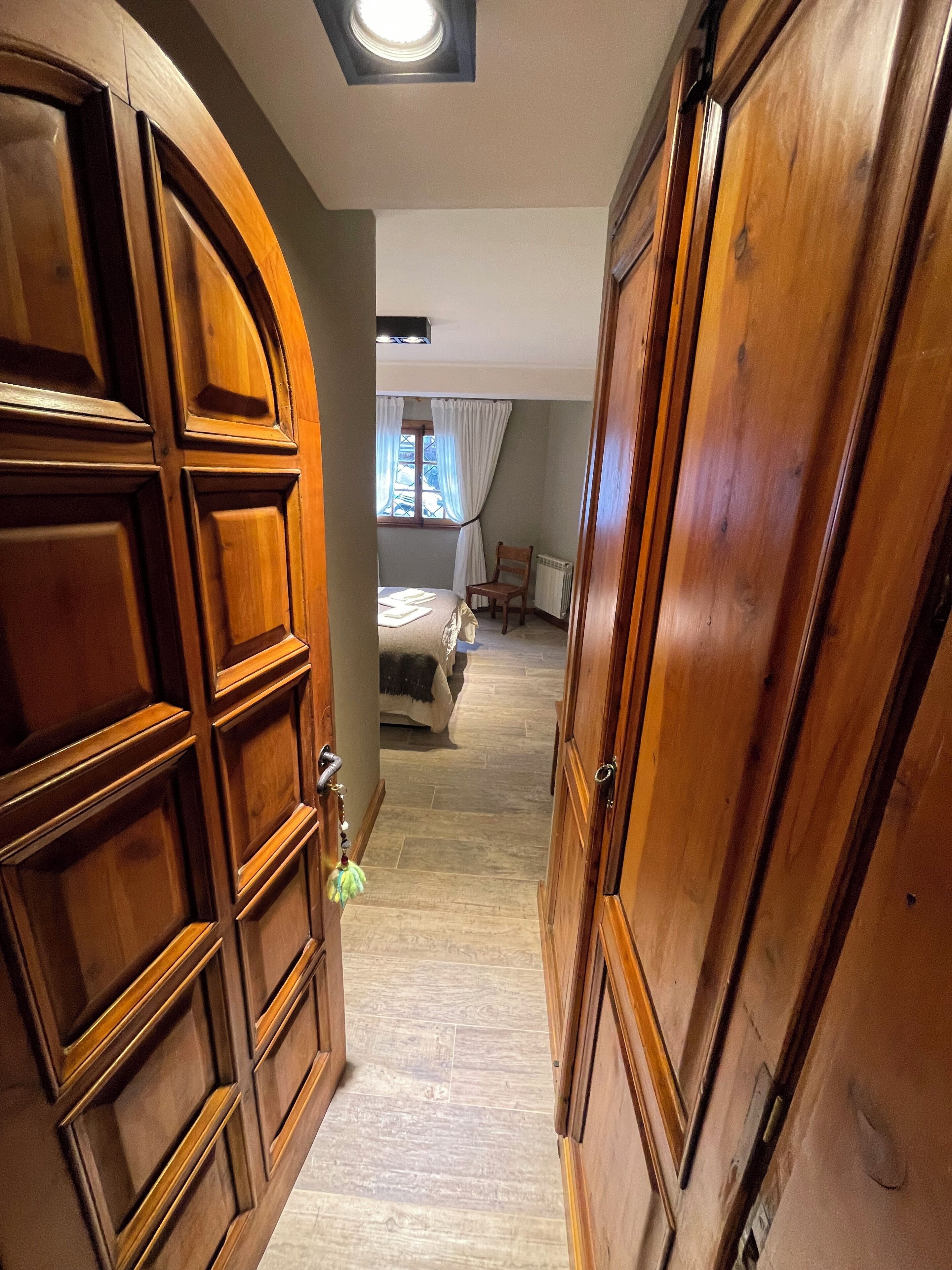 A hallway with wooden doors, a bed, and a window with curtains.