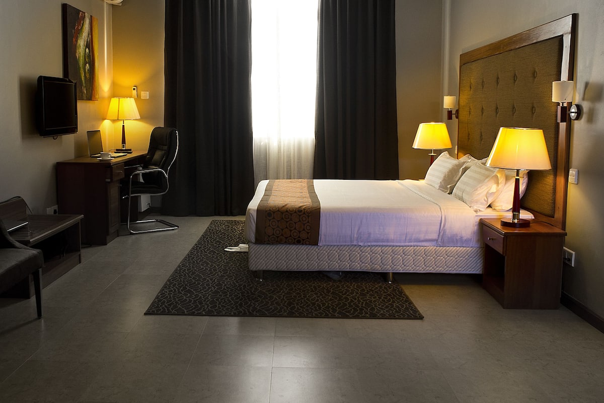 A hotel room with a bed, desk, chair, and two lamps.