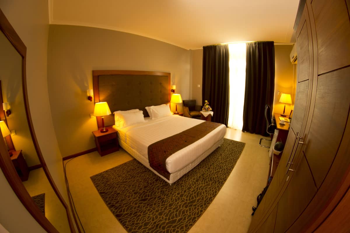 A hotel room with a large bed, two bedside tables with lamps, a wardrobe, and a mirror.