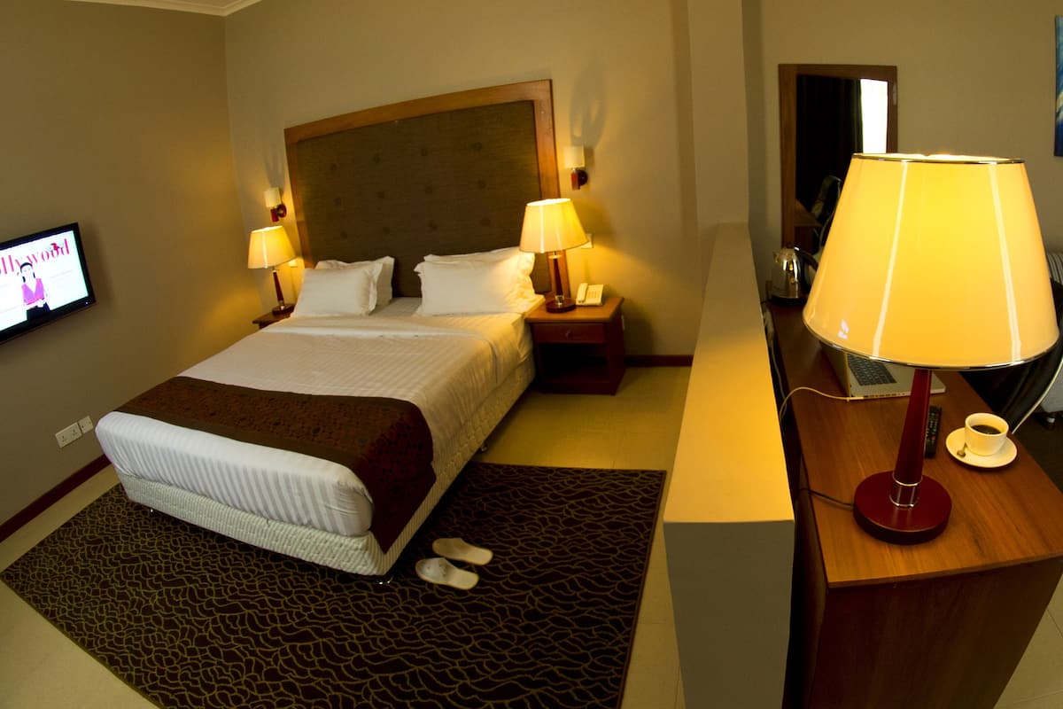 A hotel room with a bed, two bedside lamps, a desk with a lamp, a coffee table, a sofa, and a TV displaying 'Bollywood'.