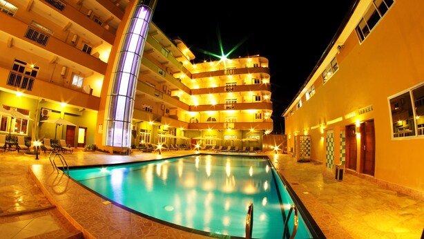 Zona de piscina con ascensor de cristal, varios balcones y fachada de edificio bien iluminada.