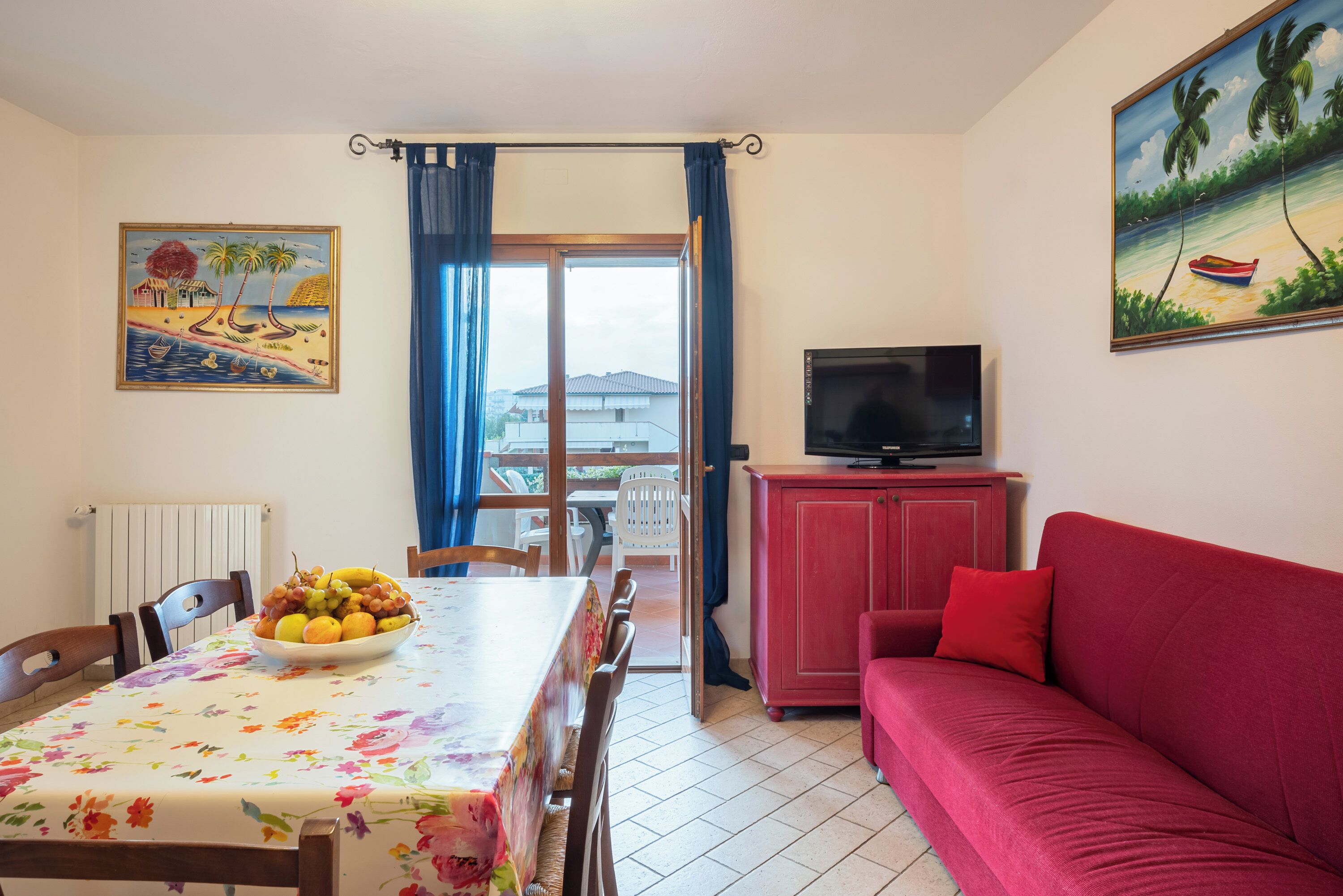 Un salón con una mesa de comedor, sofá rojo, televisor y obras de arte.