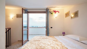 Quarto com cama, porta de correr de vidro que dá para uma varanda e vista para a cidade.