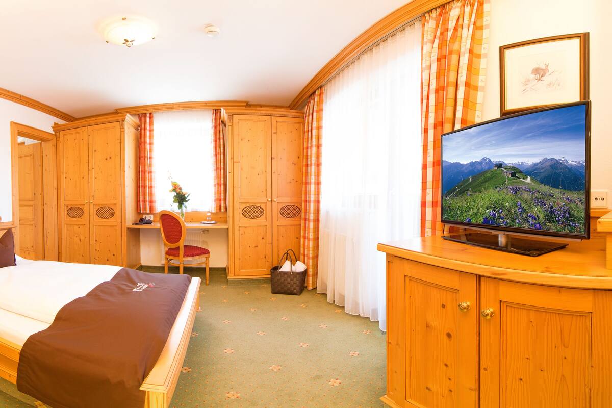 Une chambre d’hôtel équipée d’un lit, d’un bureau, d’une chaise, d’une télévision et d’armoires en bois.