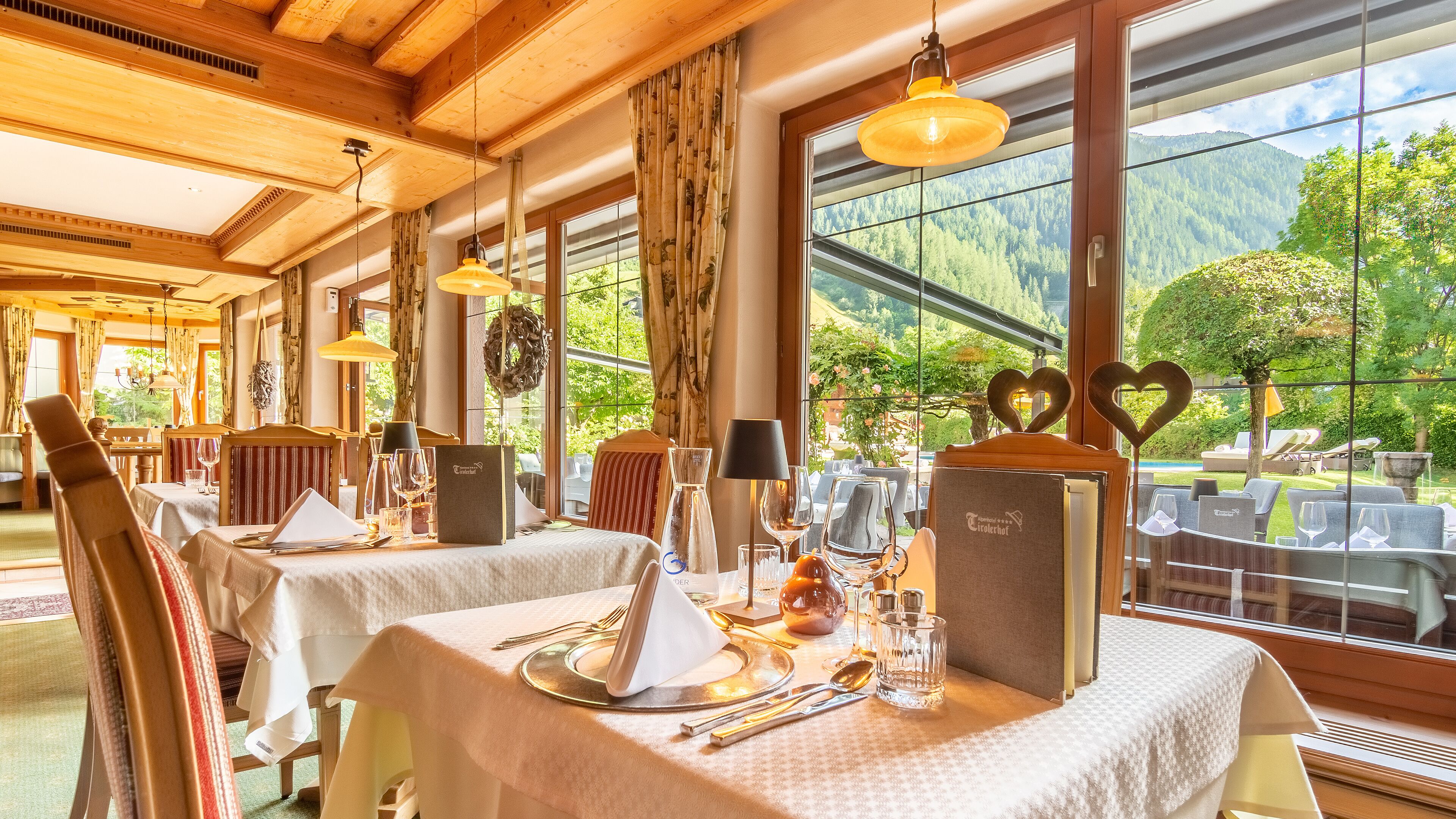 Een restaurant met houten inrichting, grote ramen en gedekte tafels.