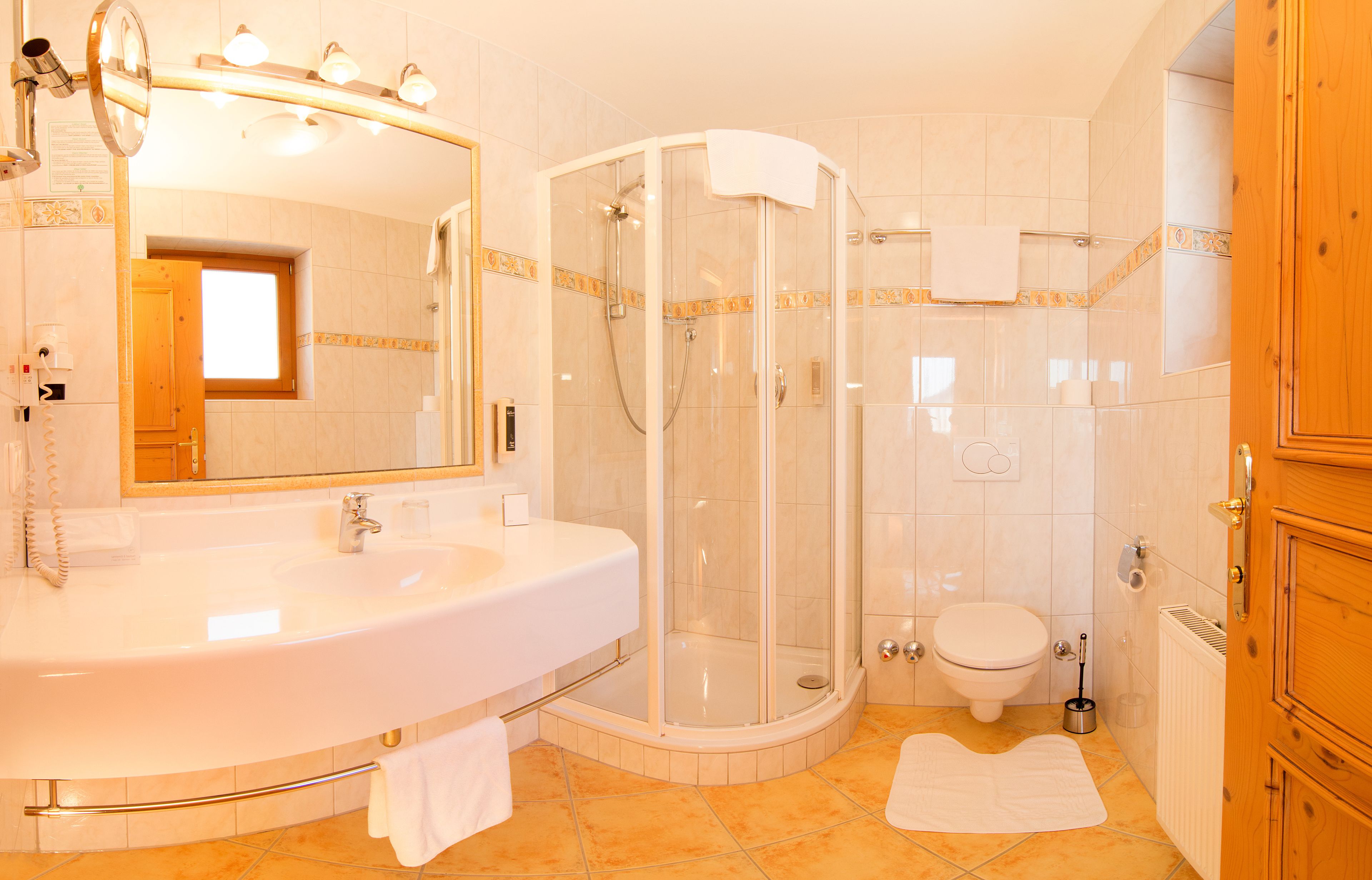 Un baño con un lavamanos grande, una ducha con cerramiento de vidrio, un inodoro y armarios de madera.