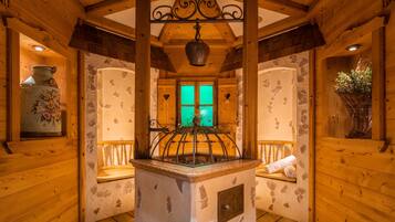 A rustic wooden interior with a stone fireplace, a hanging bell, and a window with green-tinted glass.
