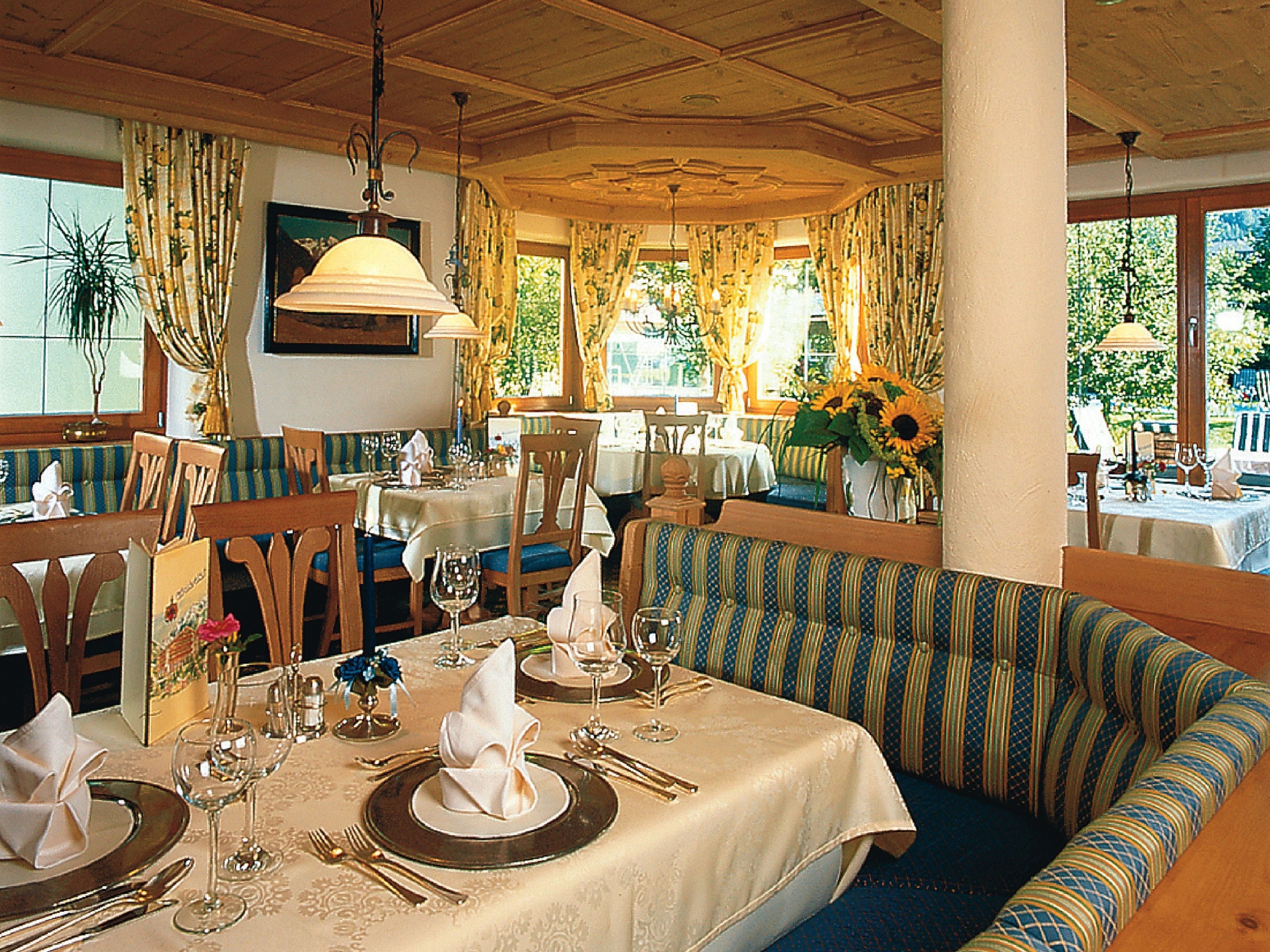 Un comedor con mesas dispuestas para comer, sillas, un banco y vistas al exterior.