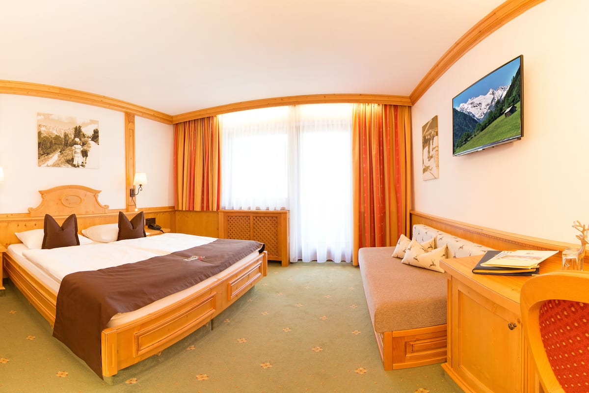 Une chambre d’hôtel avec un lit, un canapé, un bureau, une télévision et une fenêtre avec des rideaux.