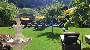 Een verzorgd gazon met een decoratieve fontein, buitenmeubels en parasols voor schaduw.