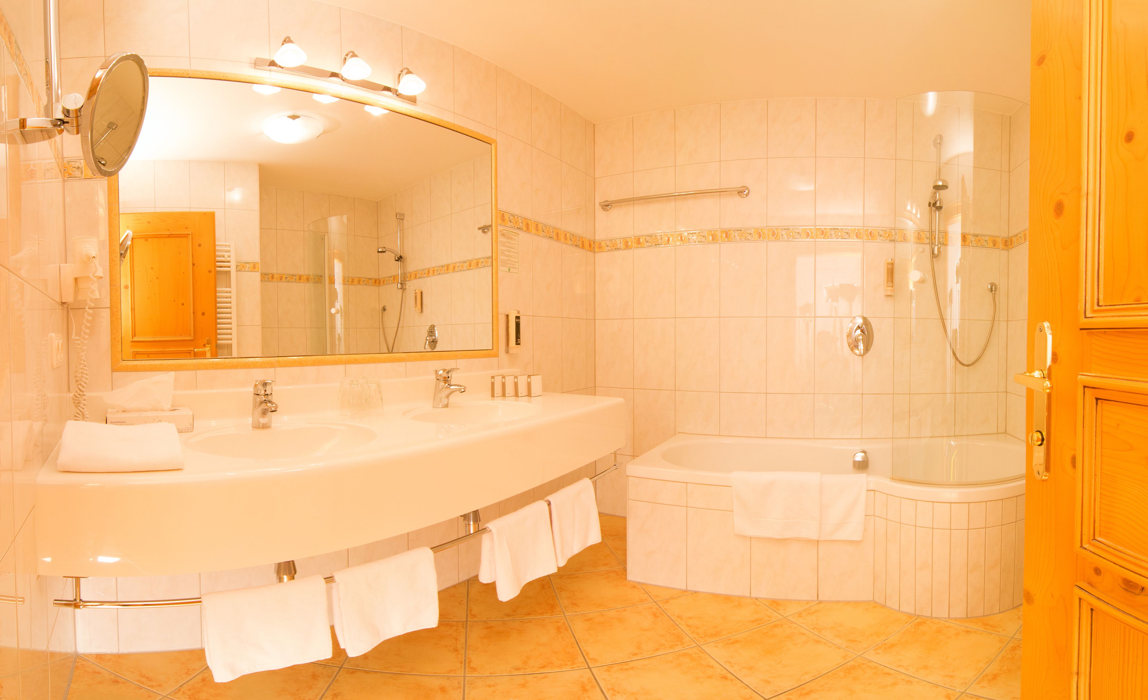 Ein Badezimmer mit zwei Waschbecken, einer Badewanne, einer Dusche und einem beleuchteten Spiegel.