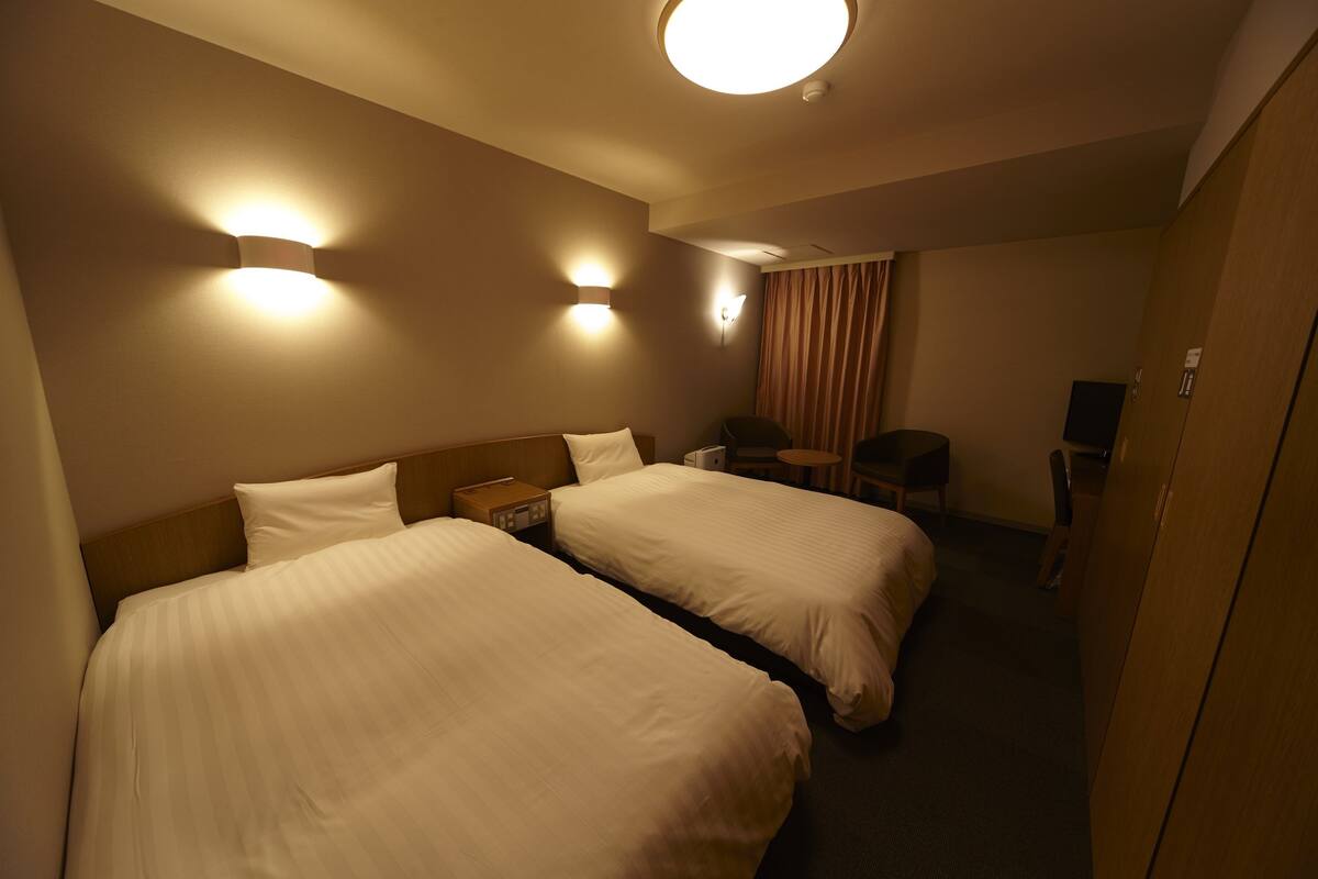 A hotel room with two beds, a desk, a chair, and a TV.