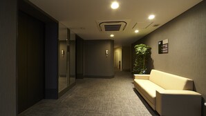 A hotel reception area with a reception desk, a waiting area with a sofa, and a plant. - Dormy Inn Express Sendai Hirosedori Hot Spring (Sendai)