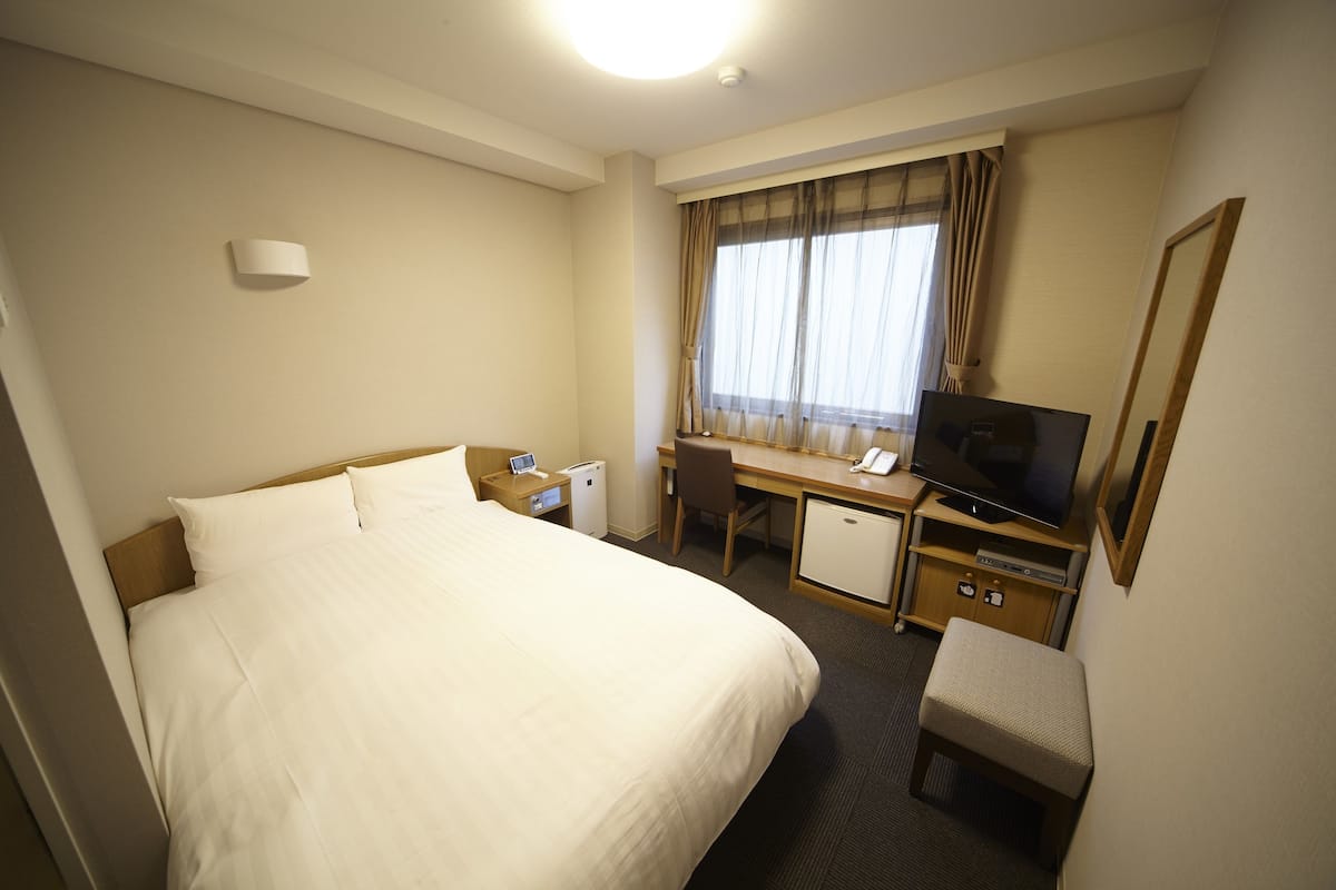 A hotel room with a bed, desk, television, and a small refrigerator.