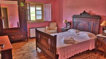 A bedroom with a wooden bed, a chair, a dresser, a nightstand, and a window with a view of greenery.