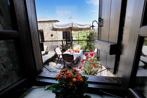 An open balcony with a table and chairs, a white umbrella, and a stone building in the background.