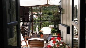 An open balcony with a view of a white umbrella, a wooden table, and red flowers. - Leonidas Village Houses (Goudi)