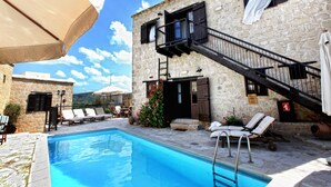 A stone building with a pool, outdoor seating, and a staircase. - Leonidas Village Houses (Goudi)