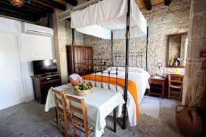 A room with a bed, a table with a basket of fruit, a television, and a stone wall.