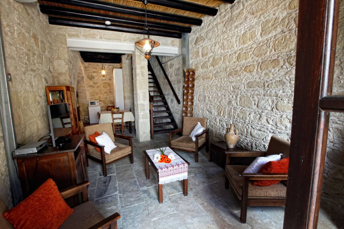 A cozy, stone-walled room with a fireplace, wooden furniture, and a staircase leading to another level.