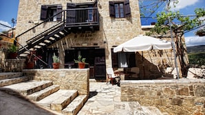 A stone building with a staircase leading to a balcony, outdoor seating, and potted plants. - Leonidas Village Houses (Goudi)