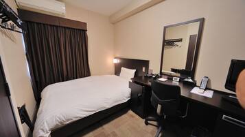 A hotel room with a bed, a desk, a chair, a desk lamp, a telephone, a mirror, and a television.