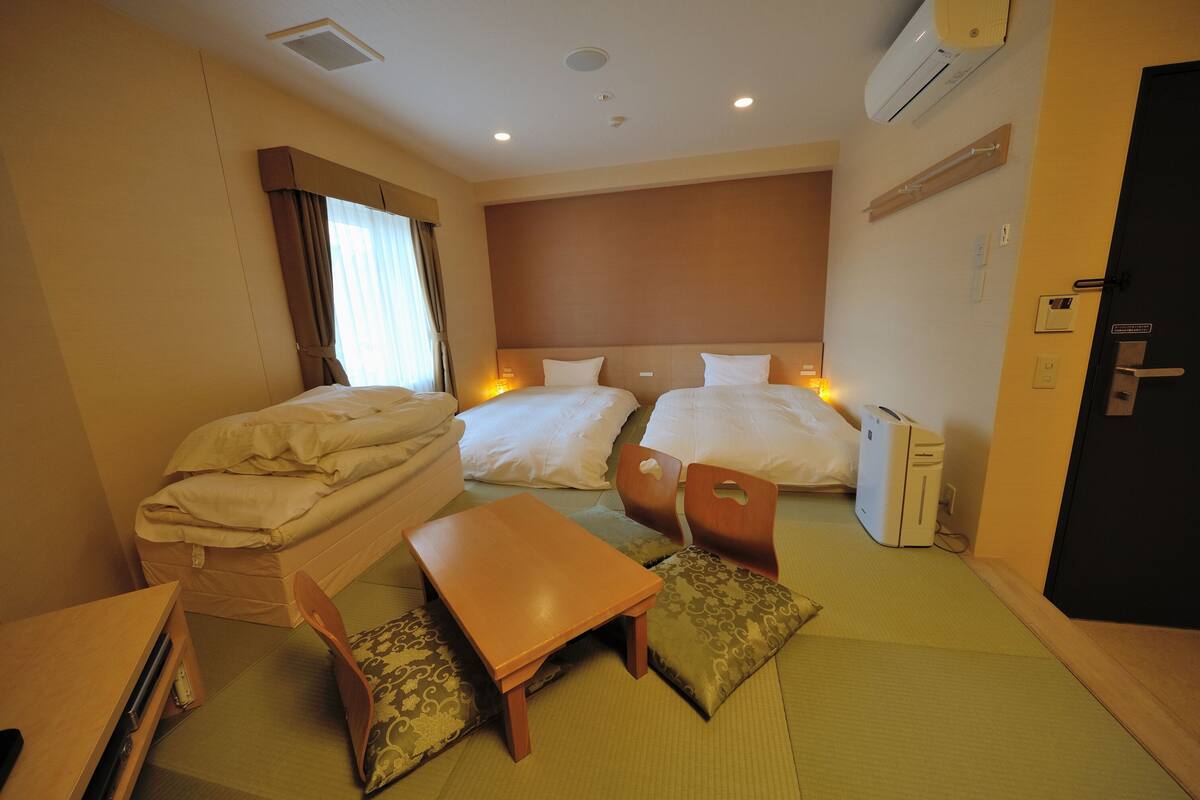 A hotel room with two beds, a small table, a chair, a desk, and a computer.