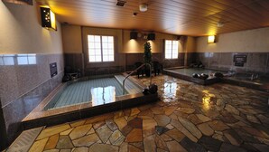Un área interior con piscina de suelo de piedra, con dos piscinas separadas, techo de madera e iluminación empotrada en la pared.