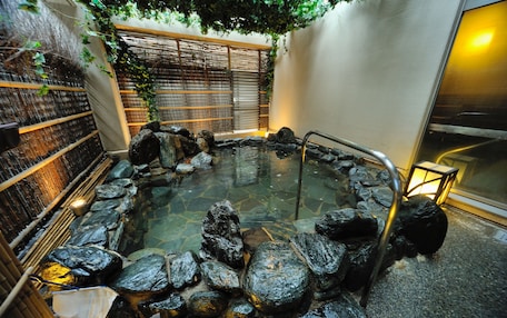 A hot spring area with a stone pool surrounded by rocks, a wooden fence, and a bamboo wall.
