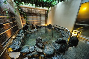 A hot spring area with a stone pool surrounded by rocks, a wooden fence, and a bamboo wall.