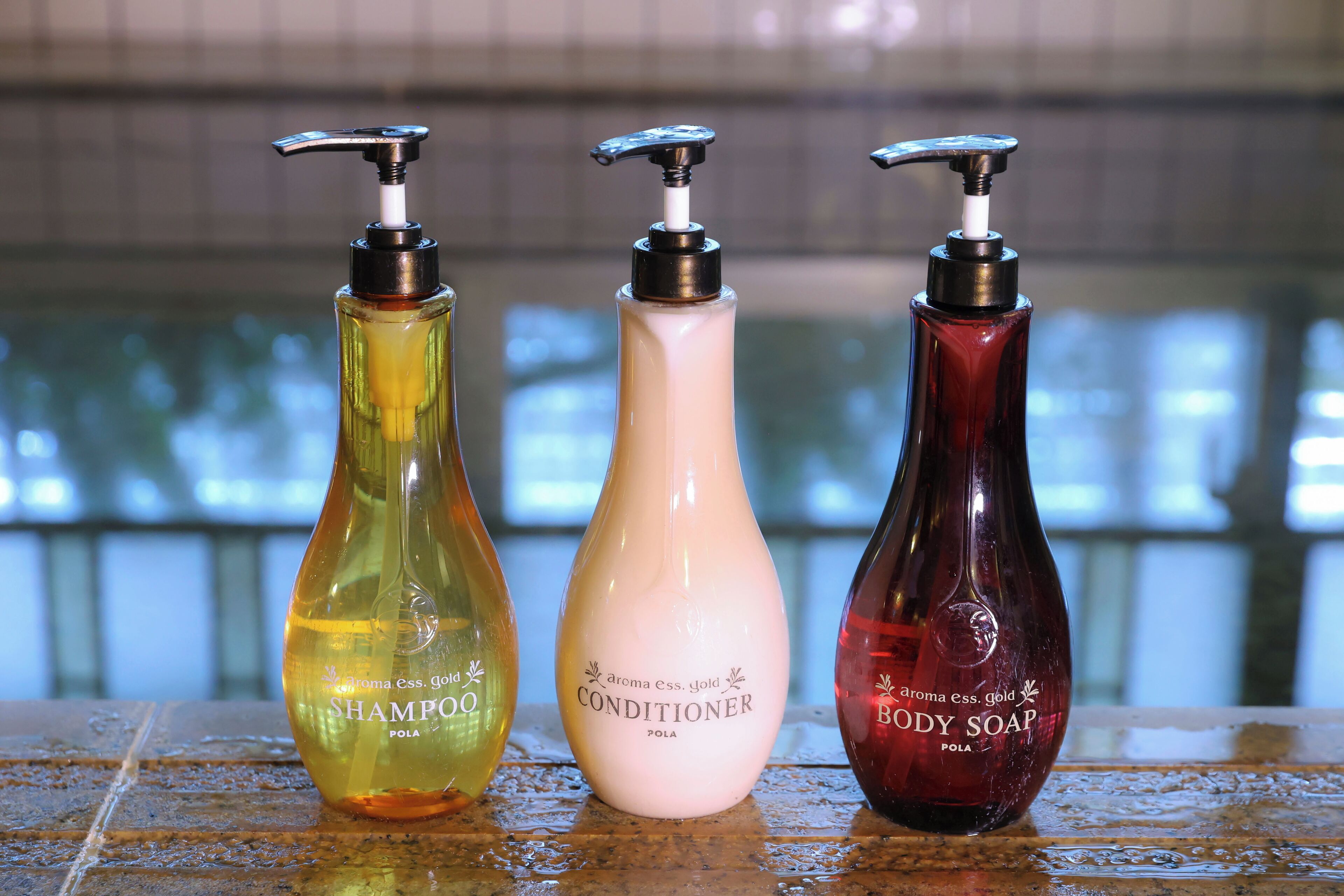 Tres botellas de champú, acondicionador y jabón de cuerpo sobre una superficie húmeda.