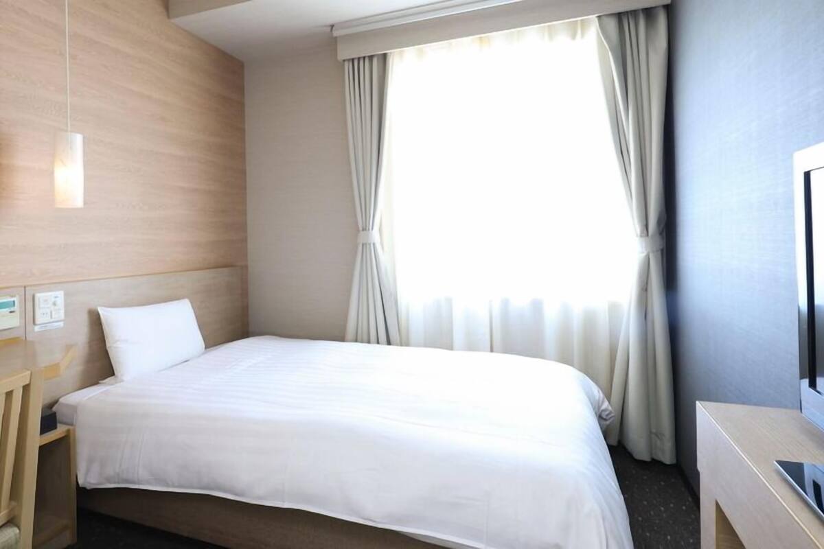Ein Hotelzimmer mit Bett, Bedienfeld, Fernseher und einem Fenster mit Vorhängen.