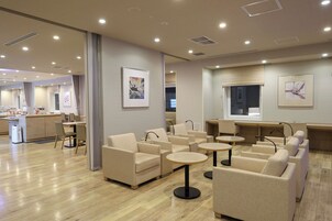 Un moderno vestíbulo de hotel con piso de madera, sofás color beige, mesas redondas y obras de arte en las paredes.