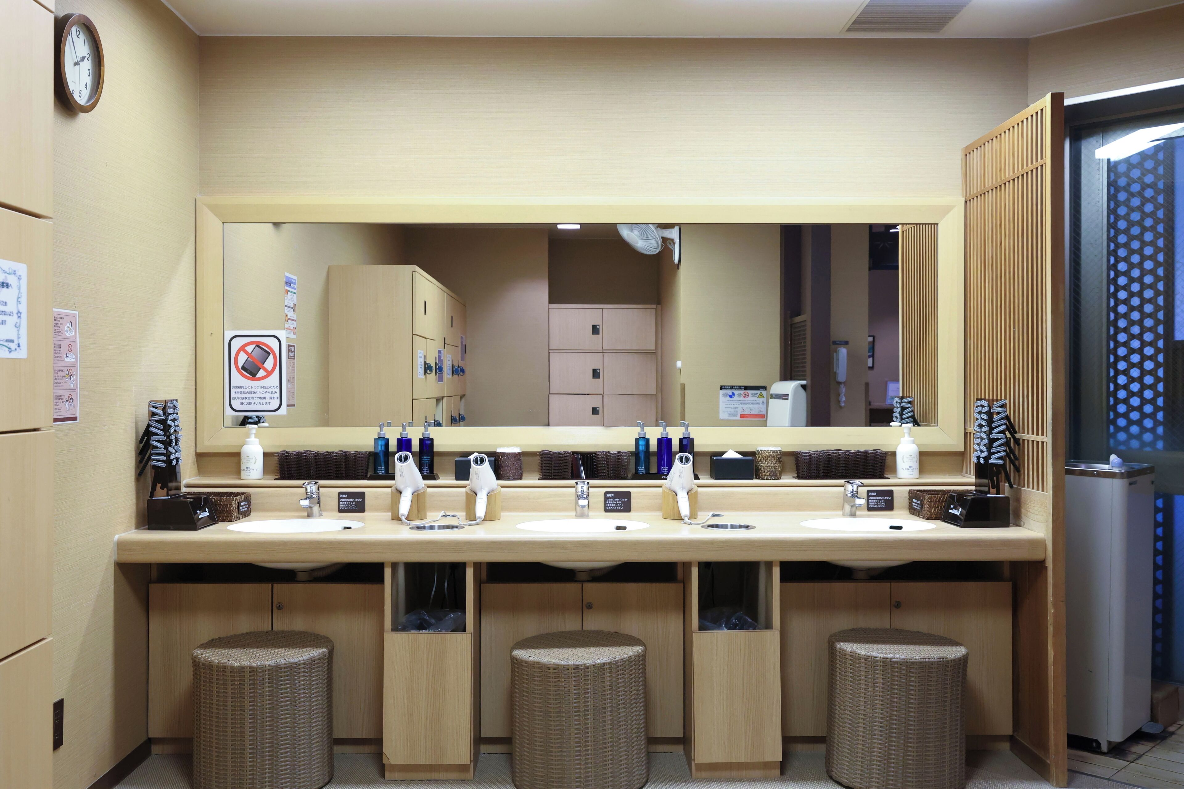 A hotel bathroom with two sinks, a large mirror, and three wicker trash bins.