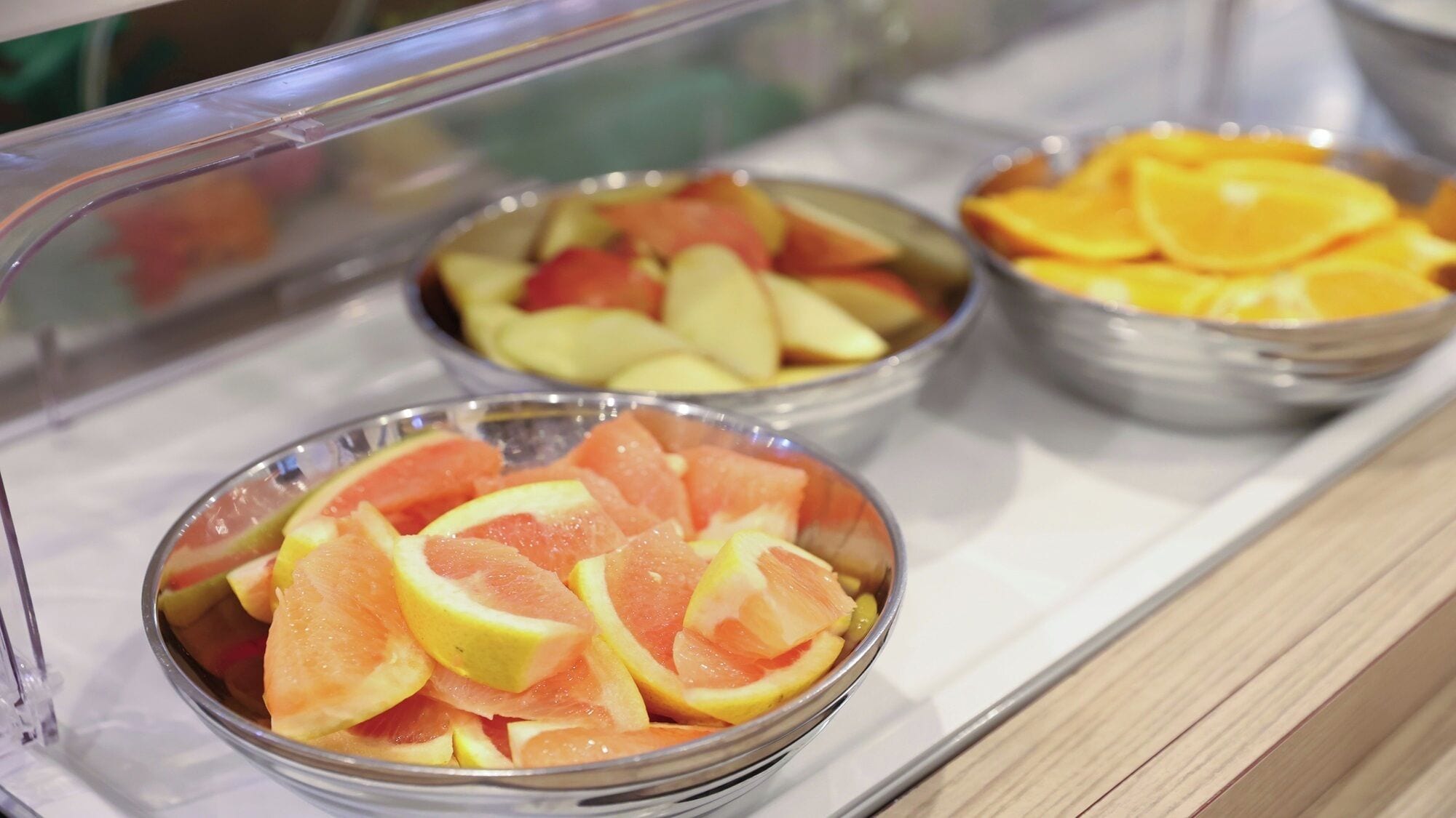 A display case with three bowls of sliced fruits.