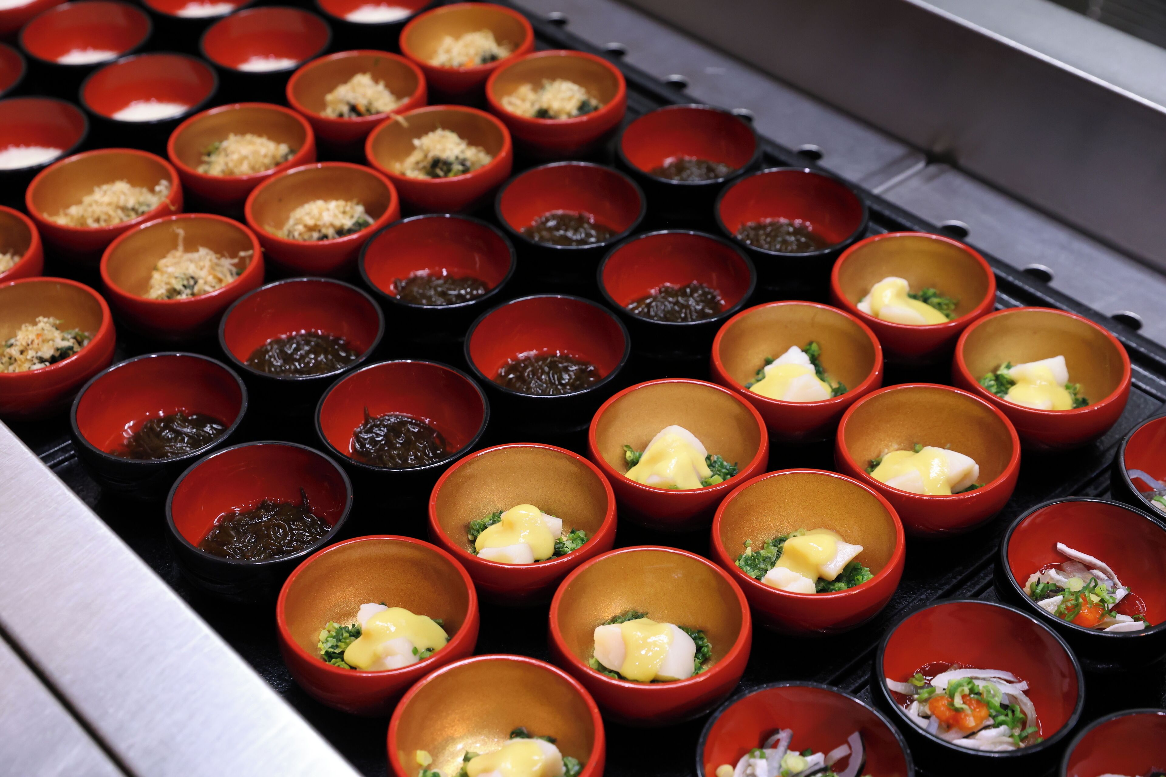 Una variedad de recipientes pequeños rojos con diferentes alimentos, dispuestos en una bandeja.