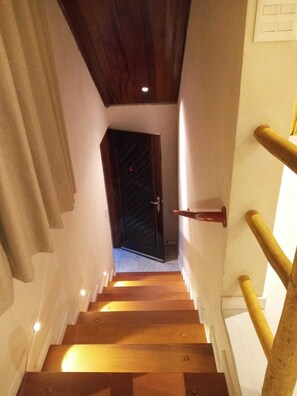 Una escalera de madera con barandilla que conduce a una puerta oscura en la parte superior.