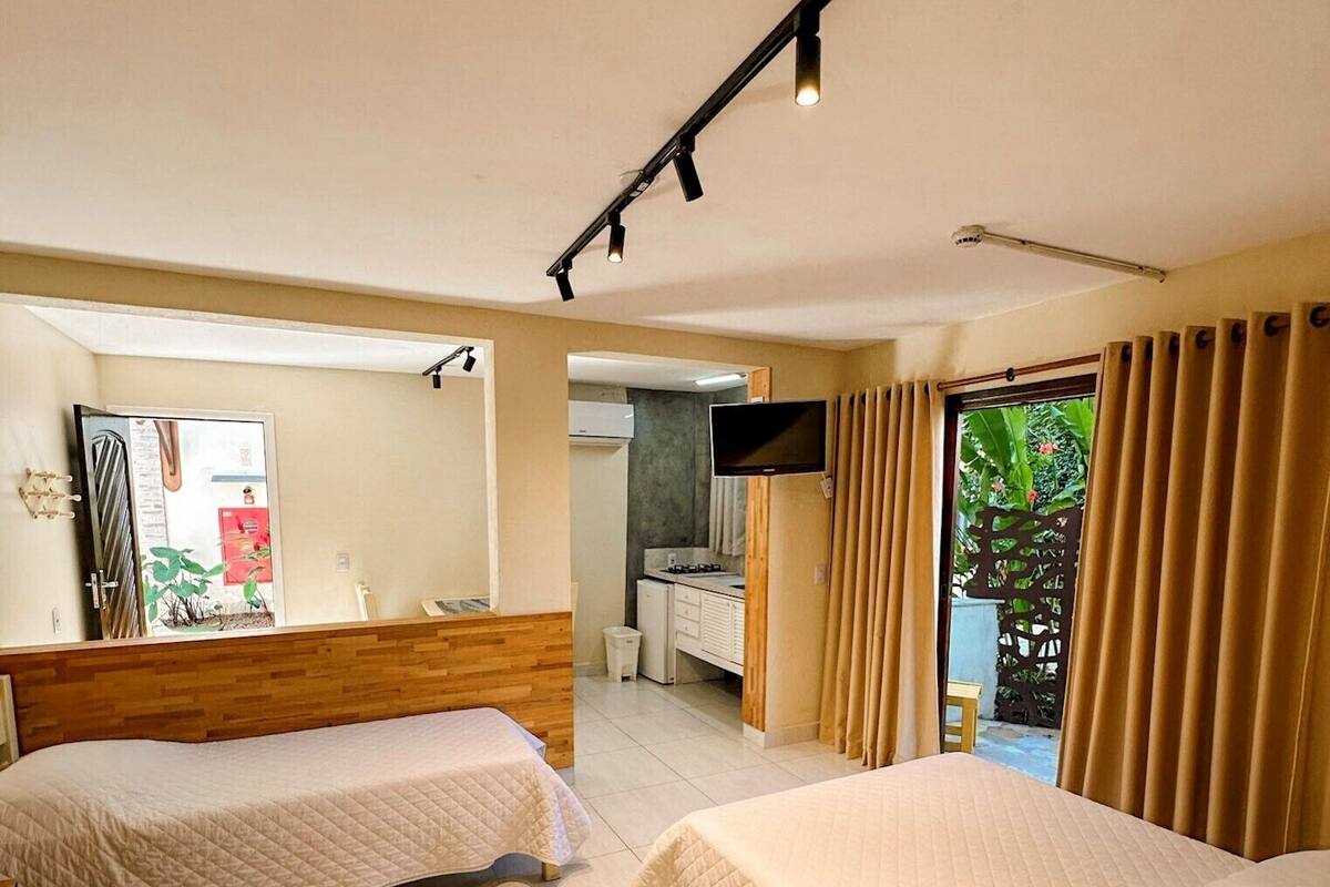 Ein Hotelzimmer mit zwei Betten, einem Fernseher, einer kleinen Küchenzeile und einem Balkon mit Vorhängen.