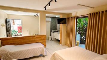 Habitación de hotel con dos camas, televisor, pequeña cocina y balcón con cortinas.