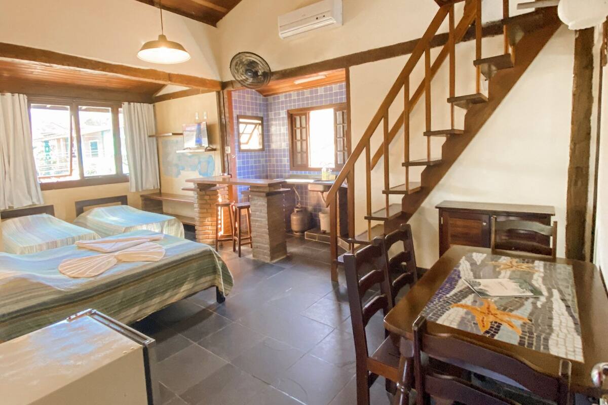 Ein gemütliches Zimmer mit Holzbalkendecke, einem Esstisch mit Stühlen, einer Küchenzeile und einer Treppe.