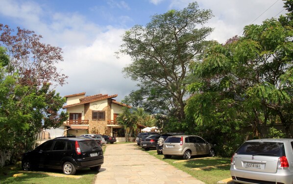 A residential street with parked cars and a house with a stone facade and tiled roof.