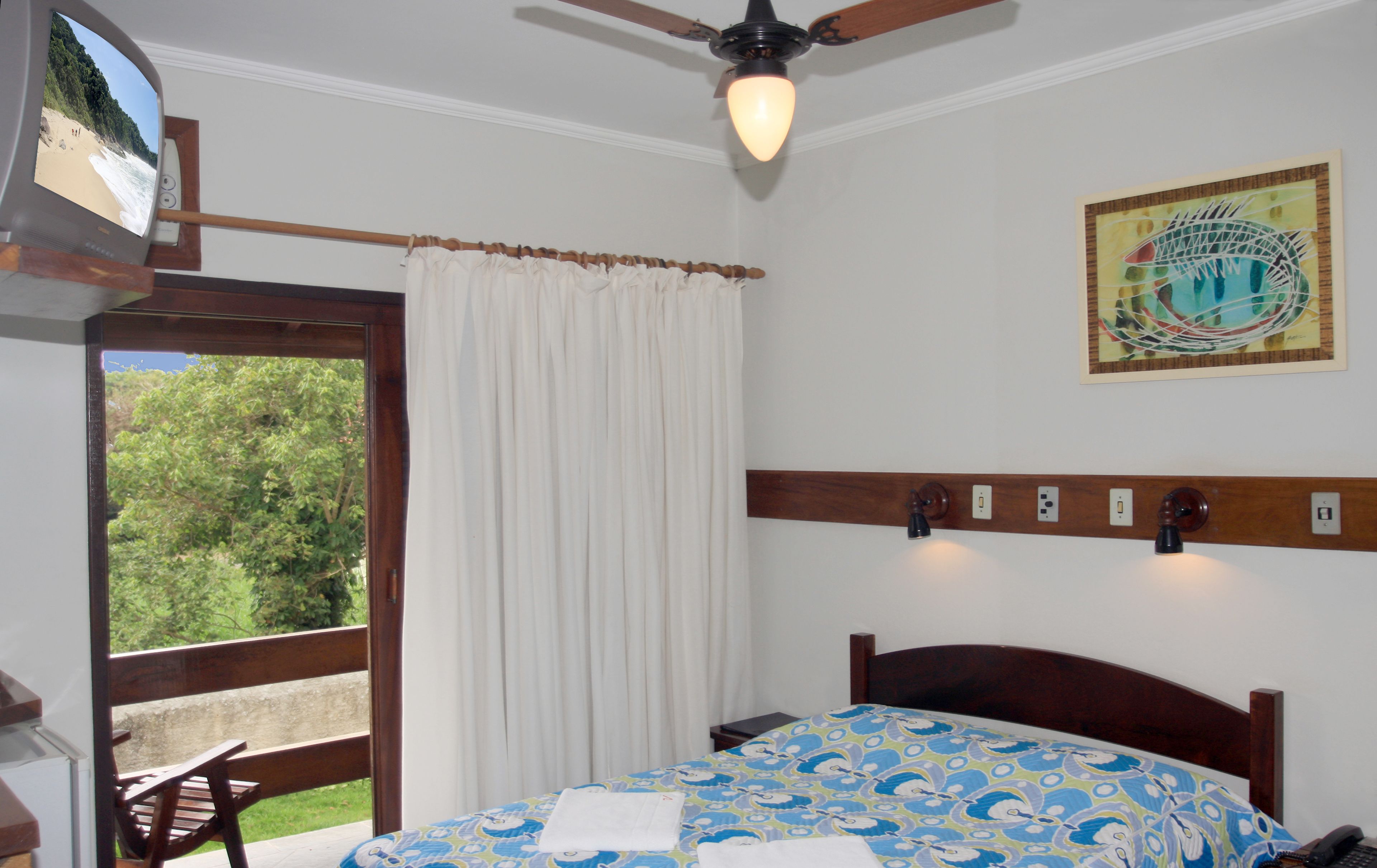 A bedroom with a bed, a ceiling fan, a window with curtains, a wall-mounted light, and a painting.