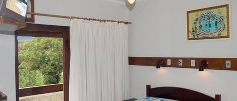A bedroom with a bed, a ceiling fan, a window with curtains, a wall-mounted light, and a painting.