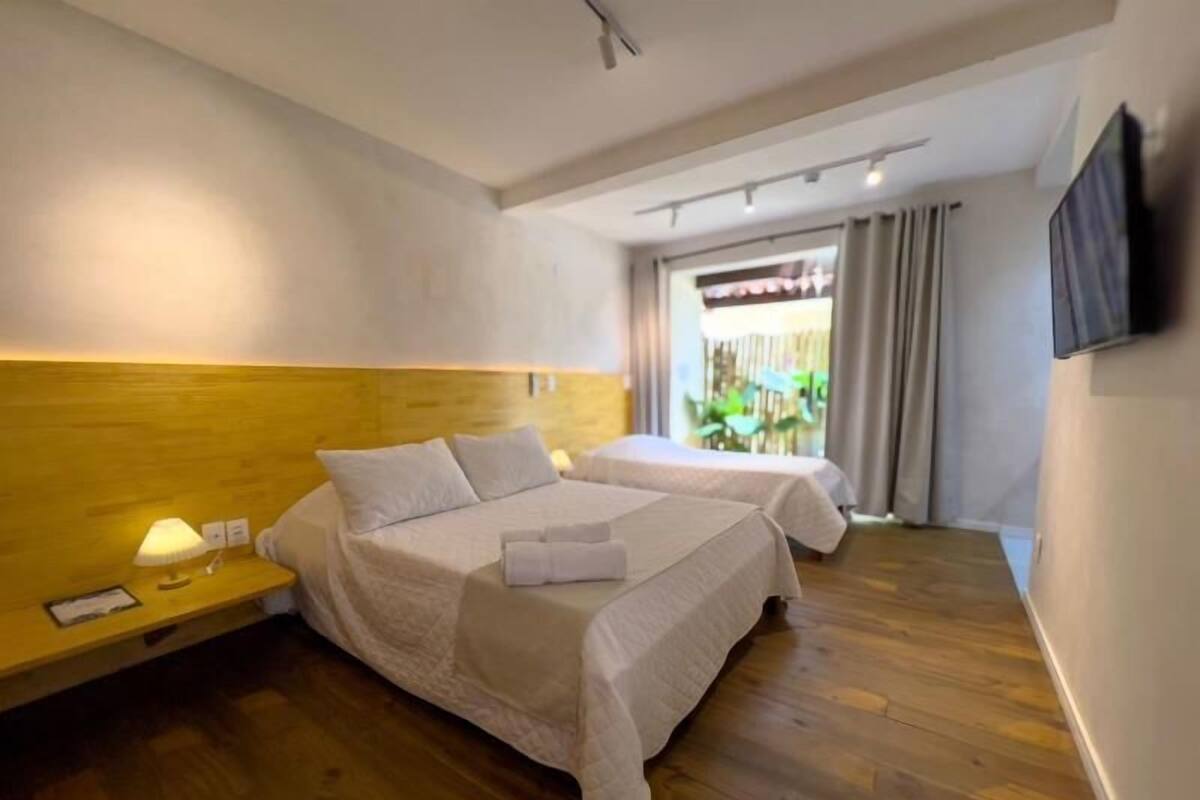 Ein Hotelzimmer mit zwei Betten, Holzboden, einem Nachttisch mit Lampe und einem Fenster mit Vorhängen.