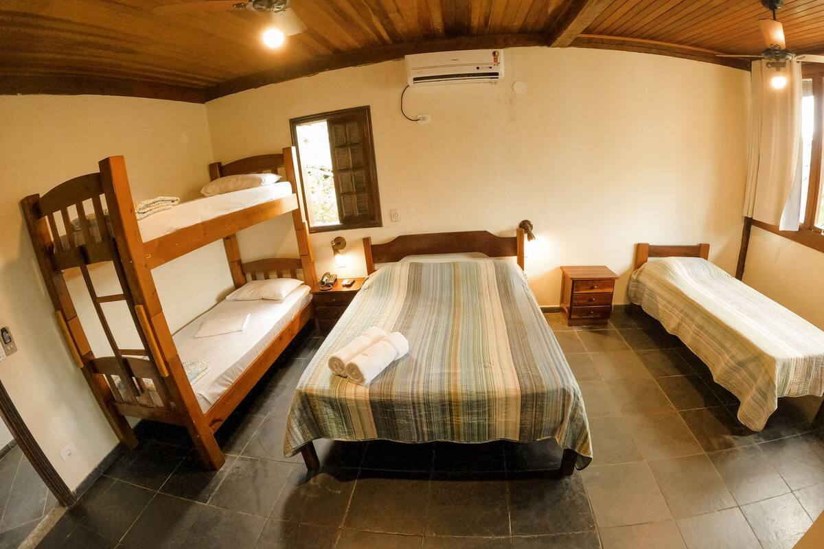 Ein Zimmer mit zwei Etagenbetten, einem Einzelbett, einem Nachttisch mit Lampe und einer Klimaanlage an der Wand.