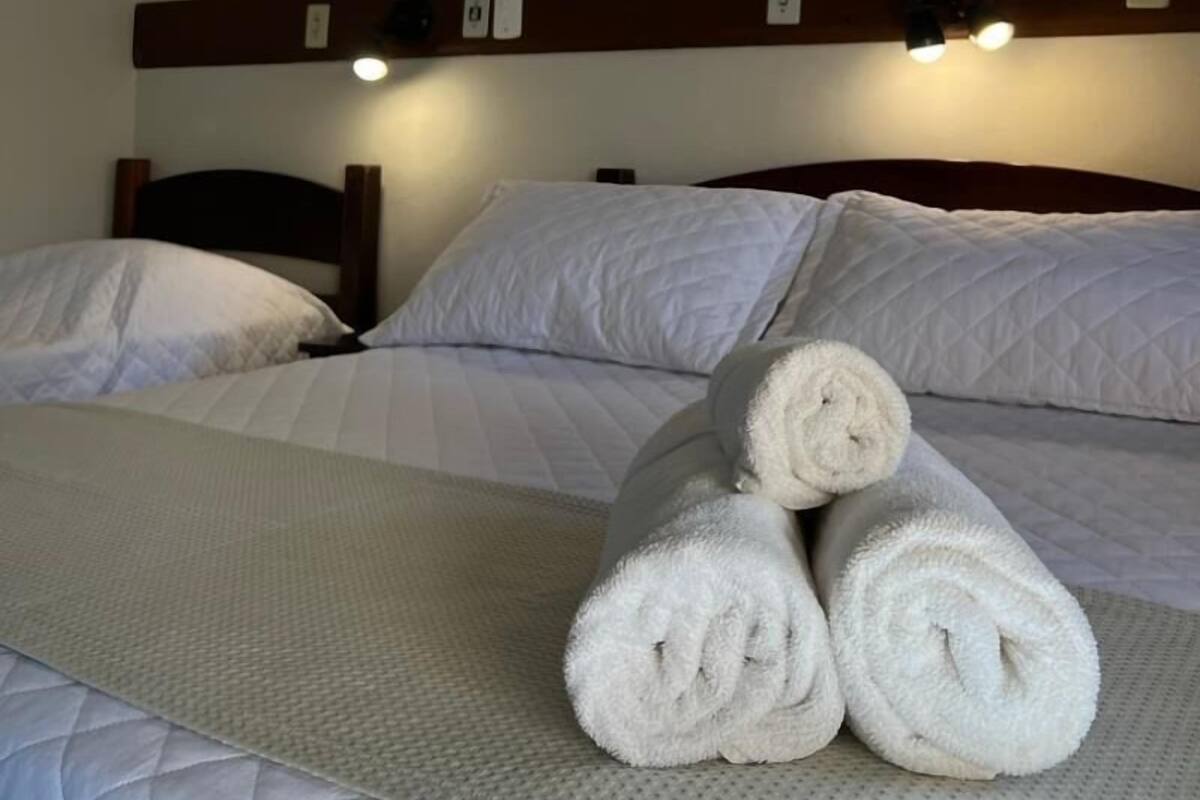 Ein Hotelzimmer mit einem Bett, zwei Kissen, einem zusammengerollten Handtuch und zwei gerahmten Bildern an der Wand.